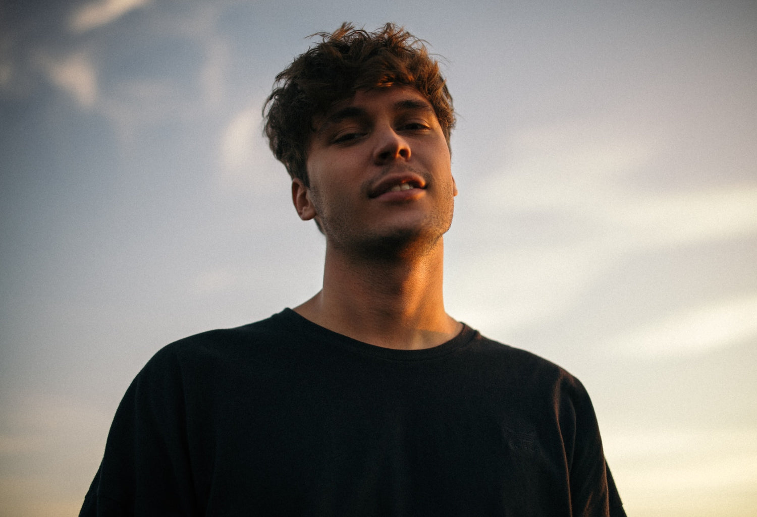 A man looking down at the camera, posing in front of a sunset